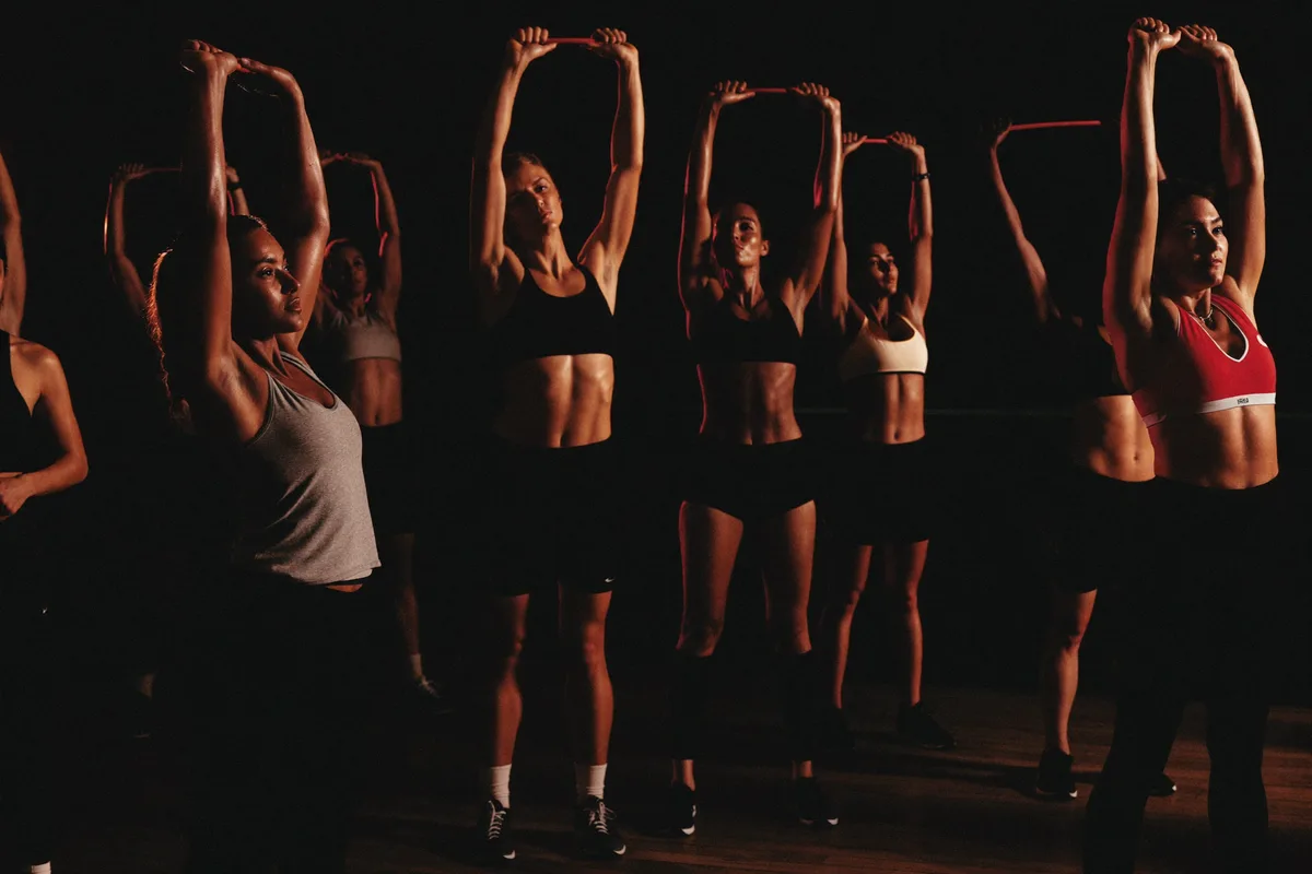 A diverse group training together in low light with a subtle coral rim light, cinematic, near-black background